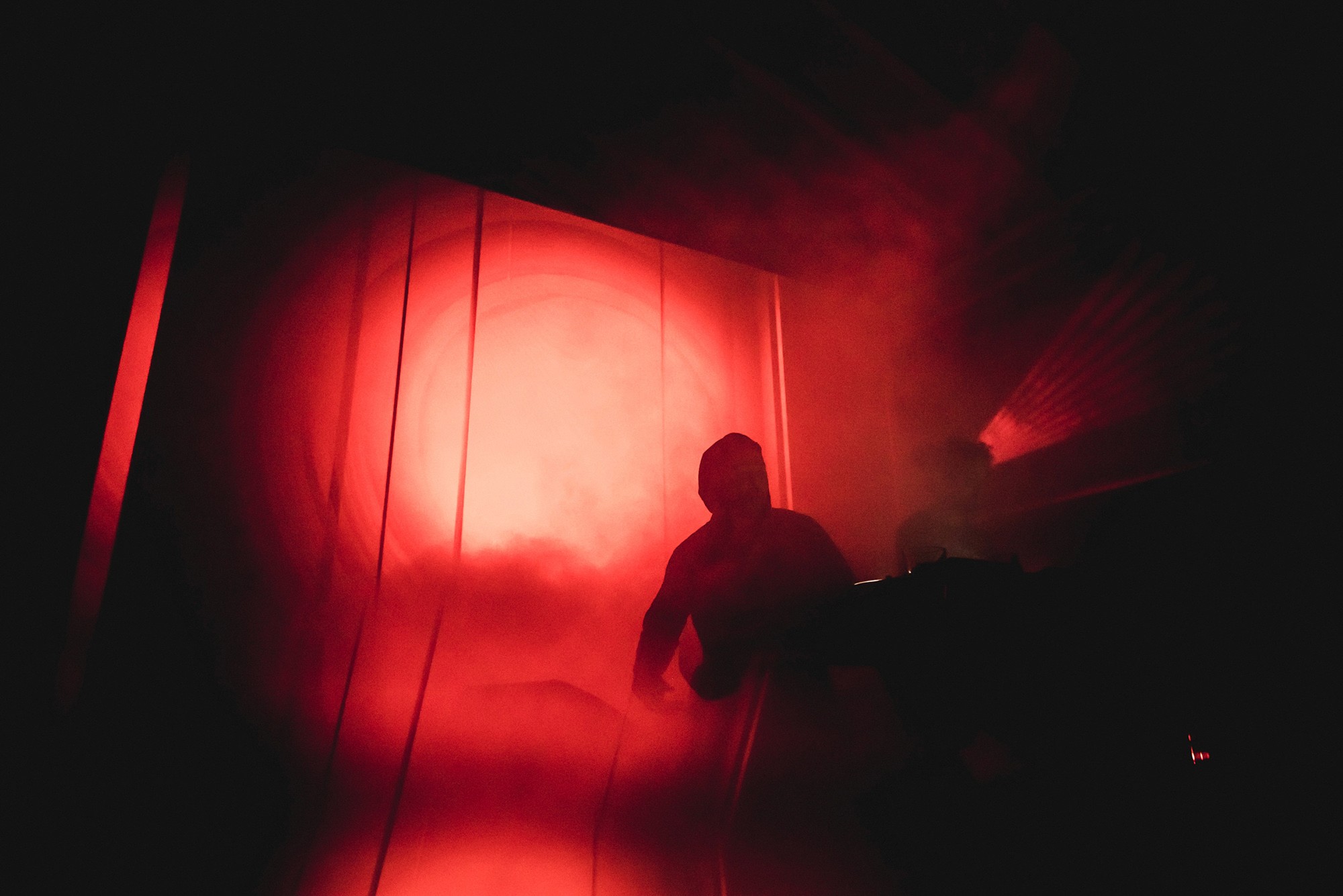 Backlit silhouette of the group Black Rave Culture on a projection of red geometric shapes.