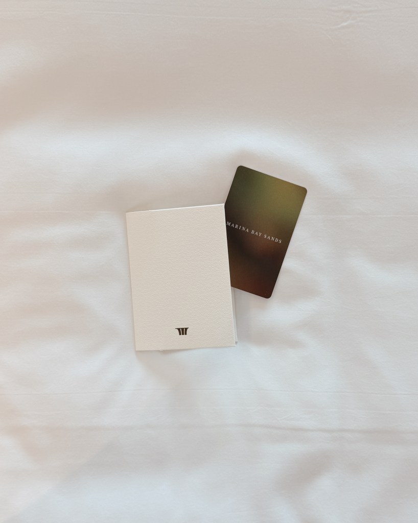 A white notebook and a Marina Bay Sands access card on a light-colored fabric surface.
