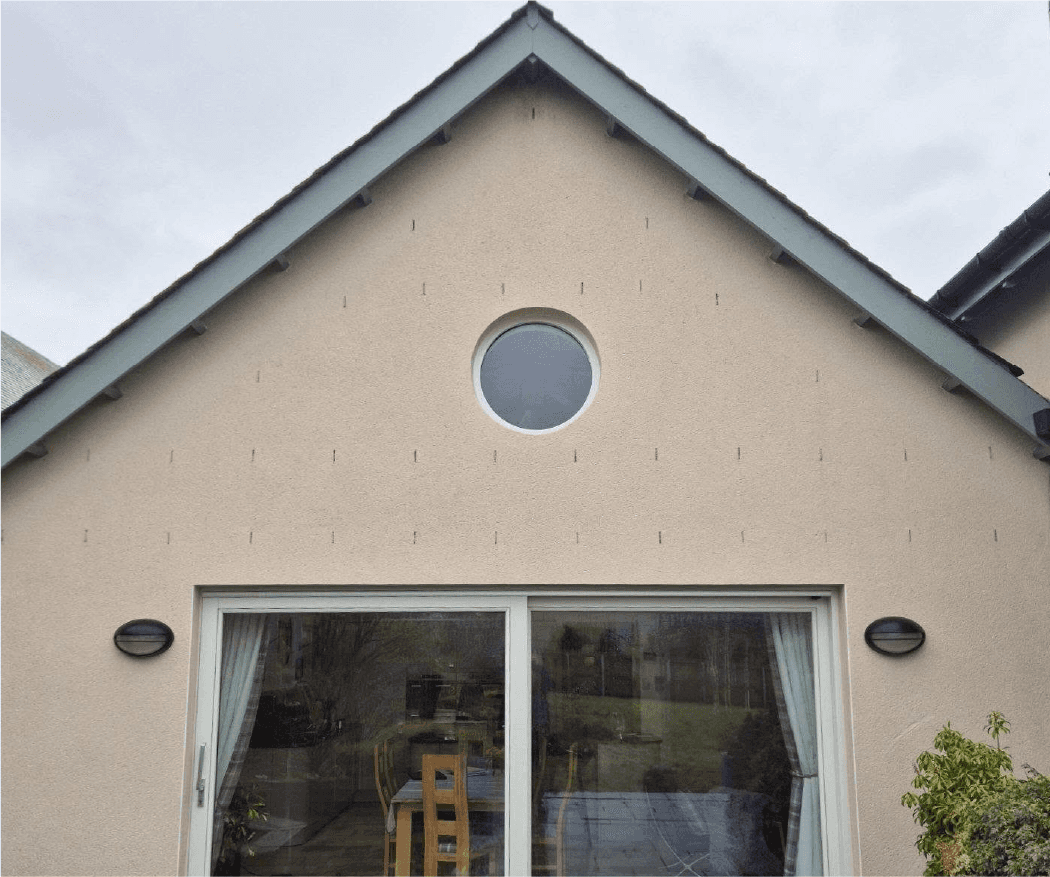 A triangular house facade with textured, clean walls features a round window with a sky reflection and a sliding glass door.