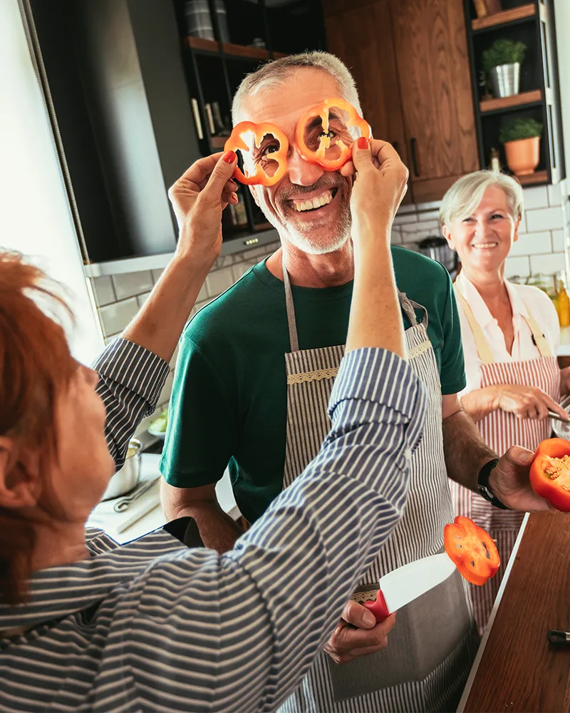 A cheerful family laughing together in the kitchen, a man playfully holding pepper rings over his eyes