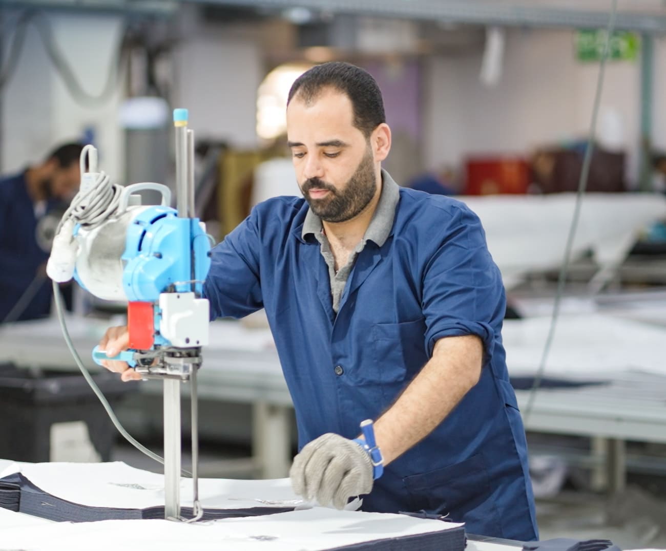Factory worker handling fabric on an industrial cutting machine.