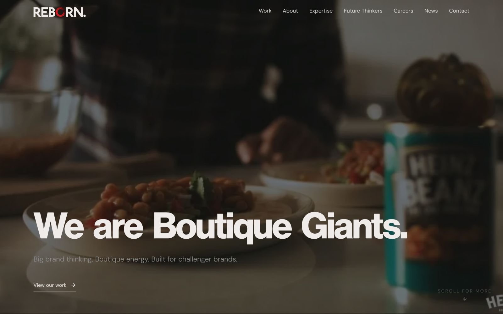 Dimly lit table with a can of baked beans, plates of food, and "We are Boutique Giants." in bold white text.