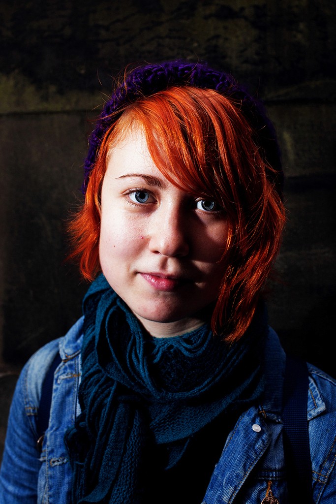 Gosia – Bitter Sweet – close-up portrait holding dark grapes near her face against a vivid blue wall