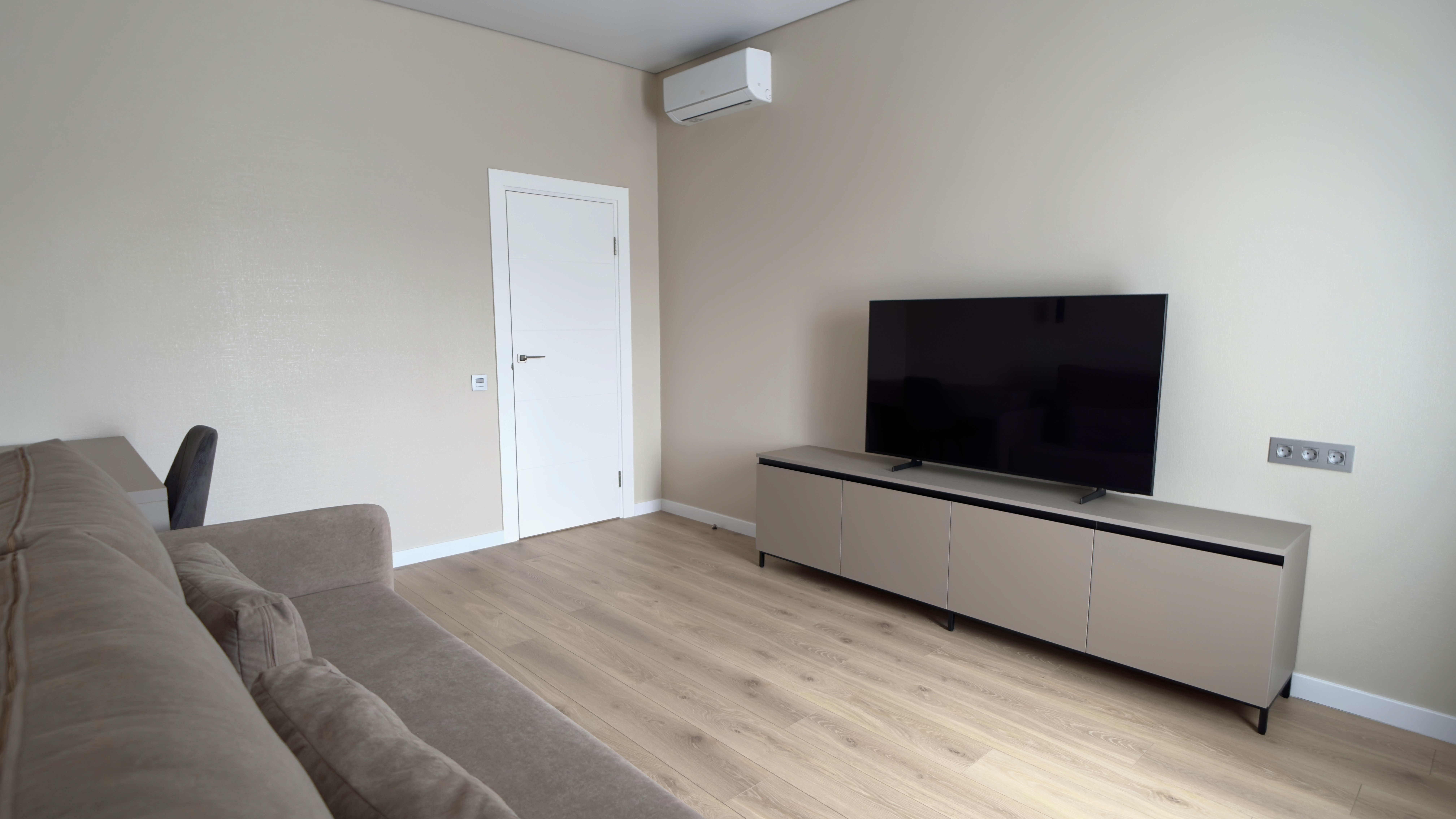 Інтер’єр кімнати з телевізором на тумбі, кондиціонером і світлими стінами