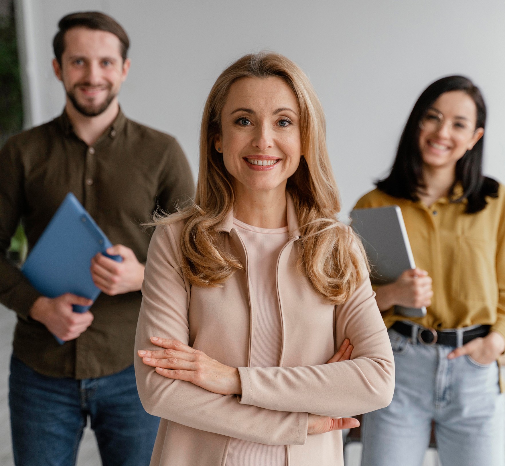 A group of three professionals smiles at the camera in a modern office setting.