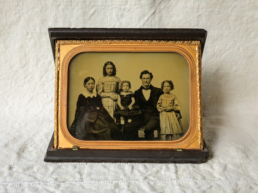 A vintage family portrait encased in an ornate frame, depicting a 19th-century family of five, highlighting historical fashion and familial bonds from a bygone era.