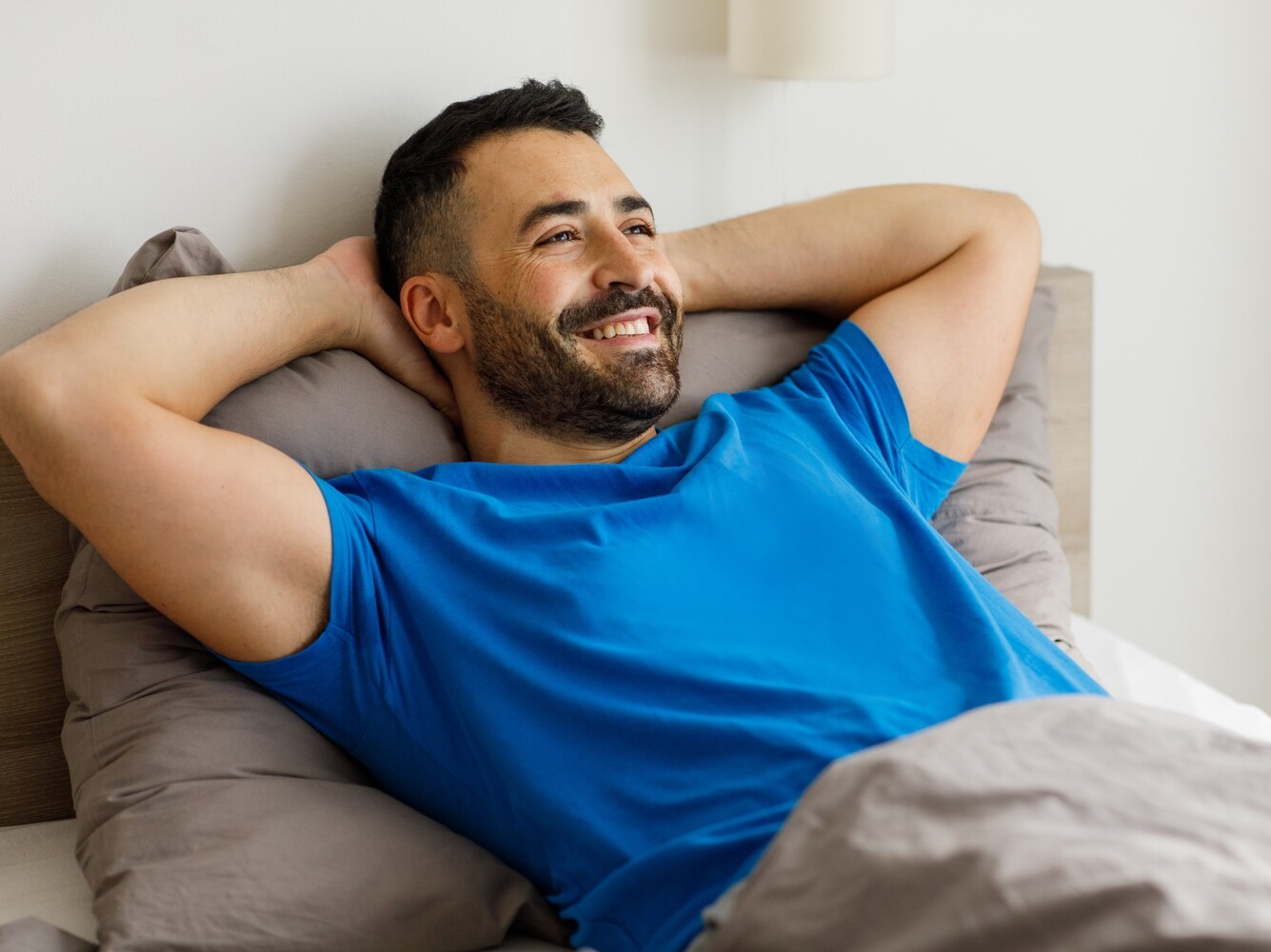 man relaxing in bed with his hands behind his head to recover from losing weight running regularly