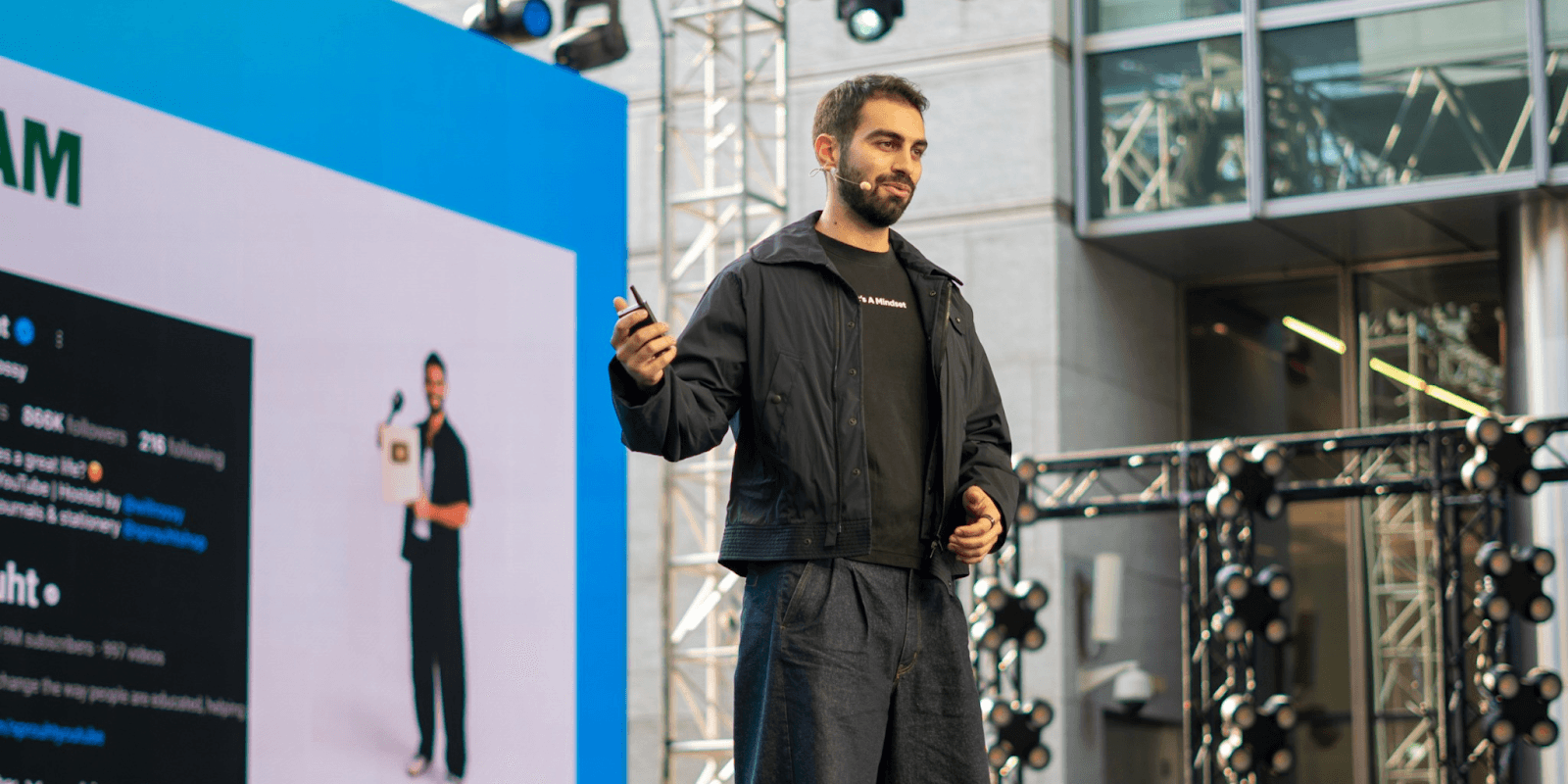 William Rossy presenting at an event, holding a phone, showcasing Sprouht’s mission of blending global wisdom and reflection.