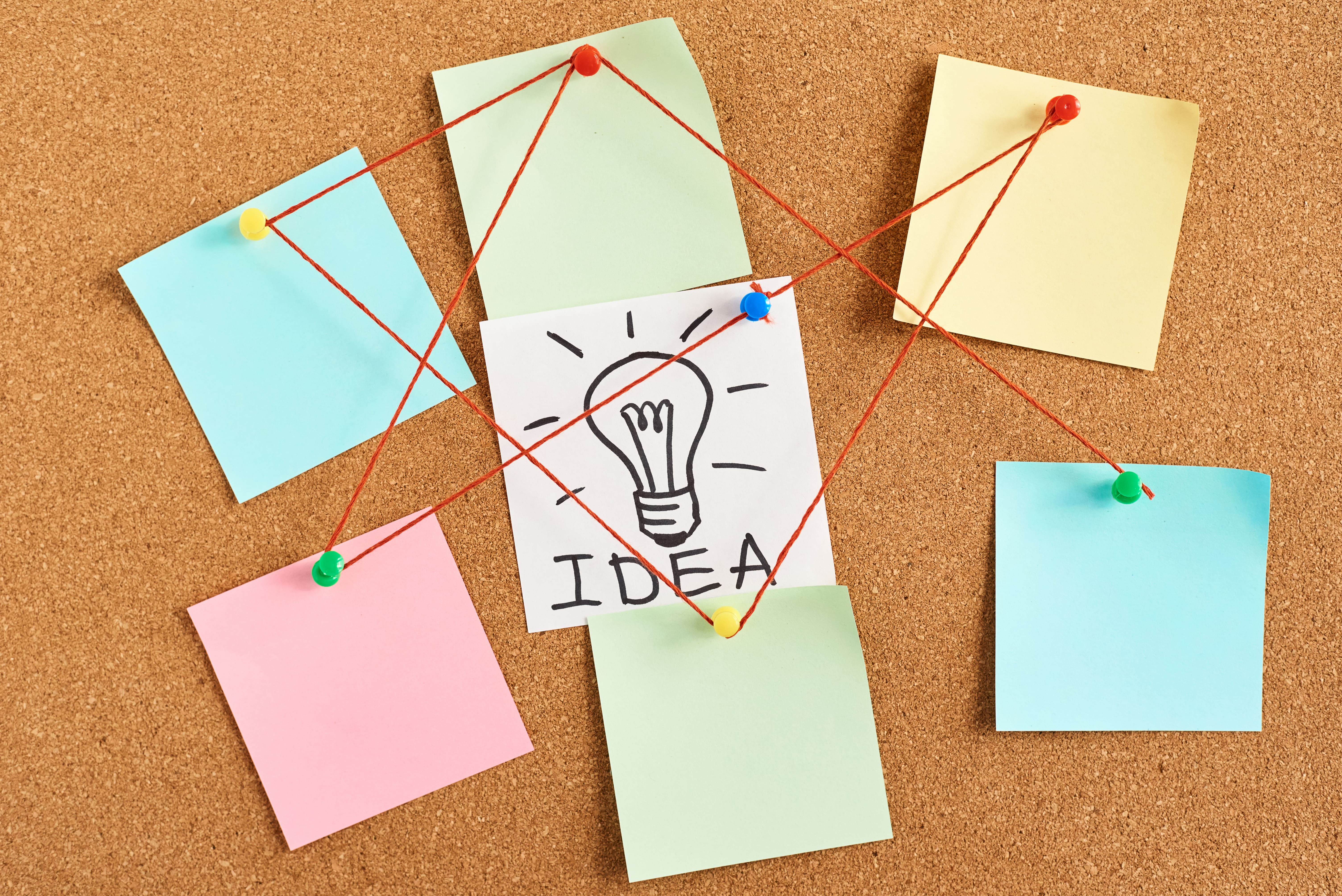 Creative idea brainstorming board with sticky notes, red thread connections, and a light bulb sketch