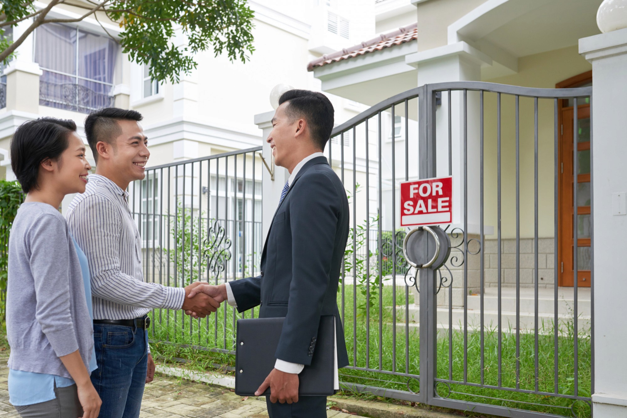 Real estate agent shaking hands with a developer or owner near a 'For Sale' sign, symbolizing property marketing and sales services.