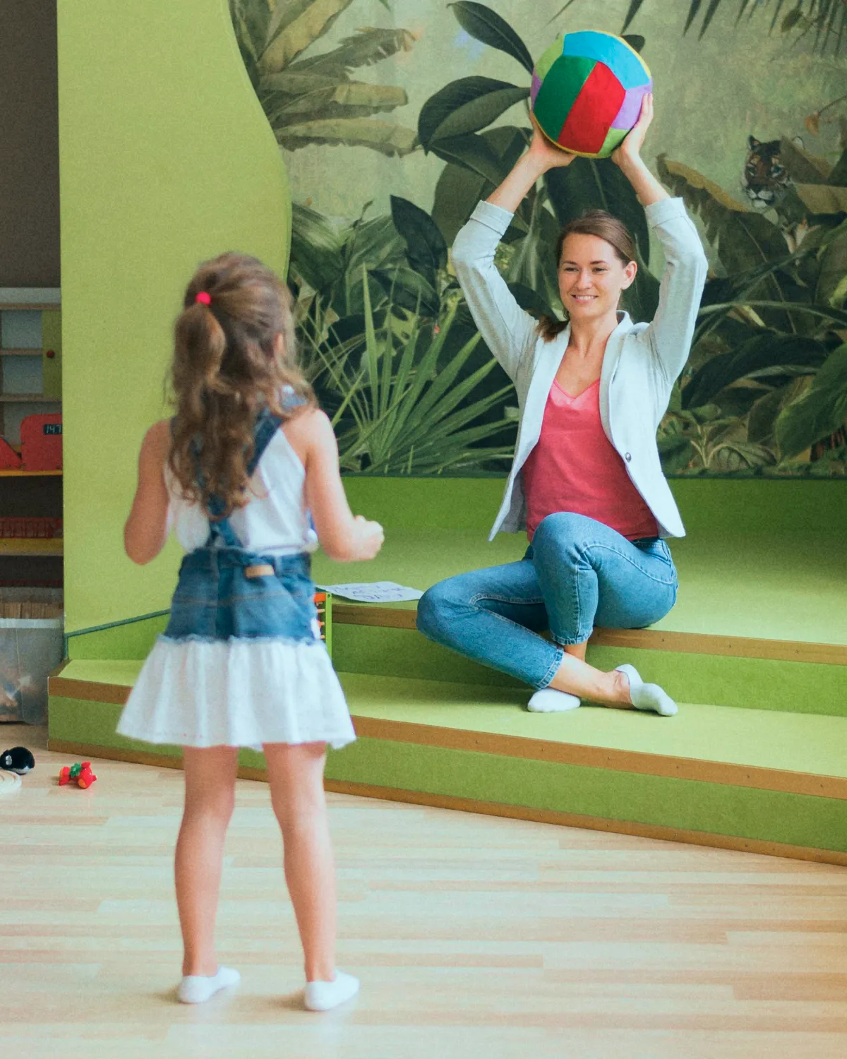 A pediatric therapist smiling while holding a colorful ball up for a young girl during a therapy session