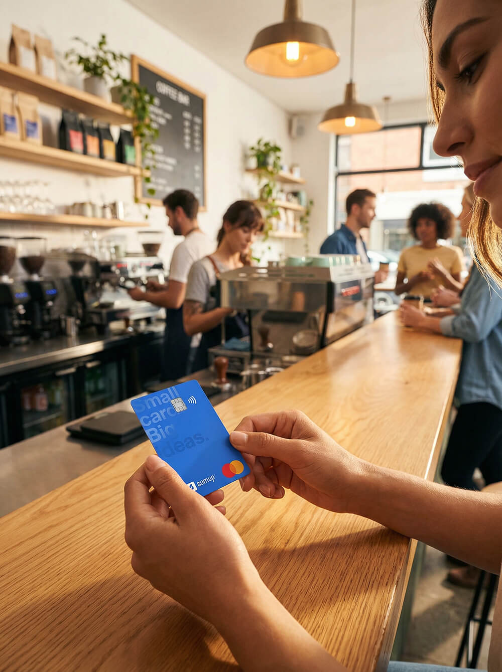 Photo of a merchant holding a SumUp debit card at a café counter, with baristas working in the background, representing real-world card usage in a small business setting.