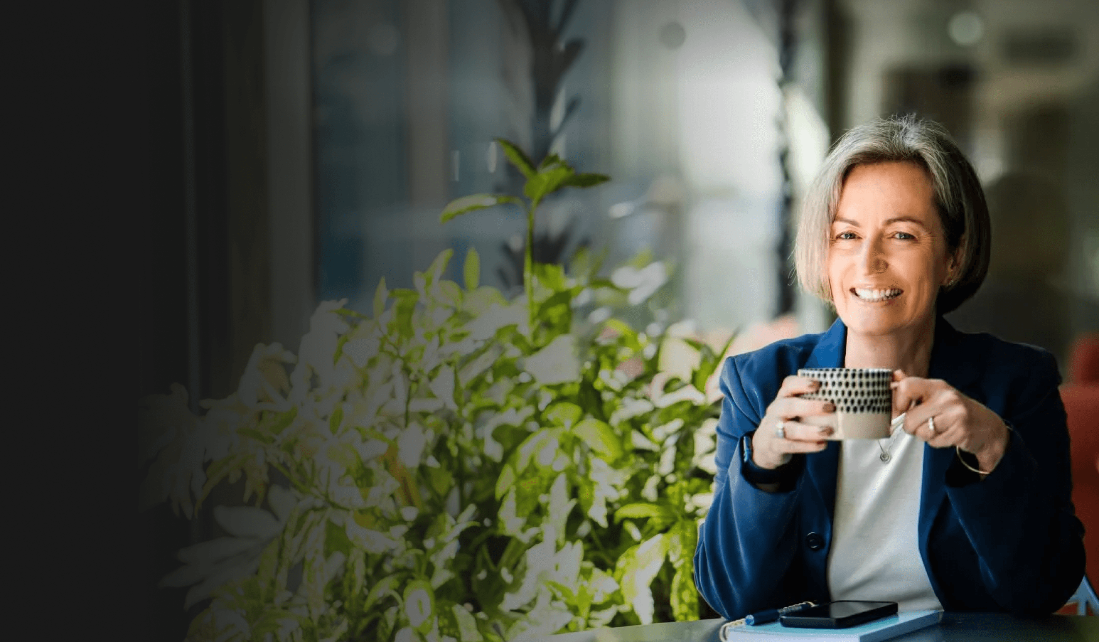 Kate sitting with a tea cup in hand with some greenery in the background