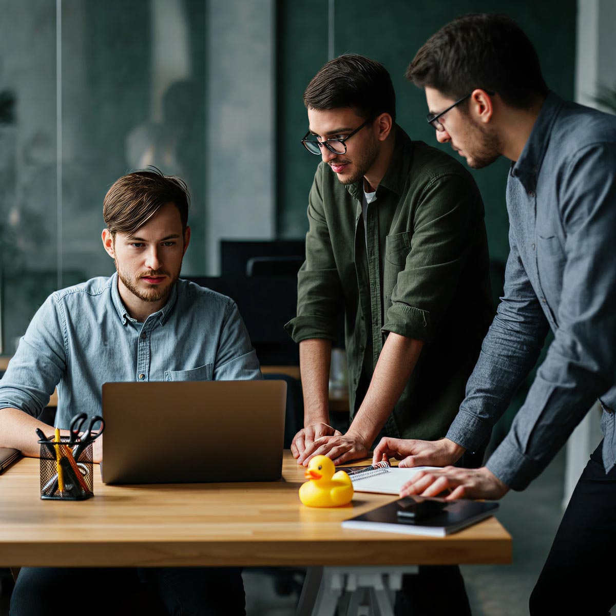 Three developers collaborating at a desk with a rubber duck on the desk
