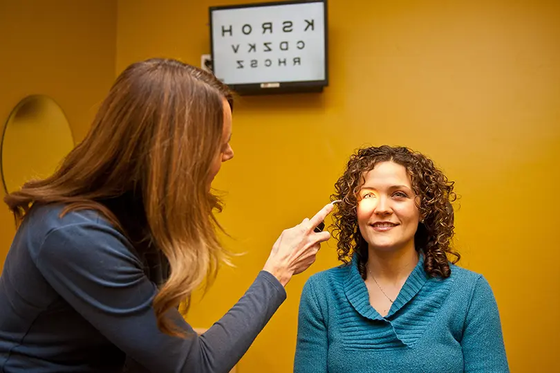 Optometrist Dr Ward performing an eye exam on a patient with eye chart in the background