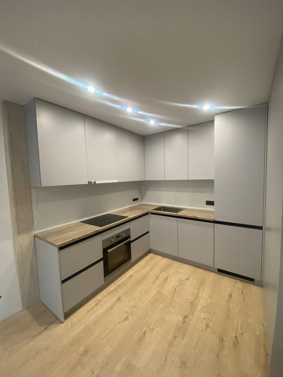 Світла кухня з підсвіткою зверху і прихованими ручками фасадів