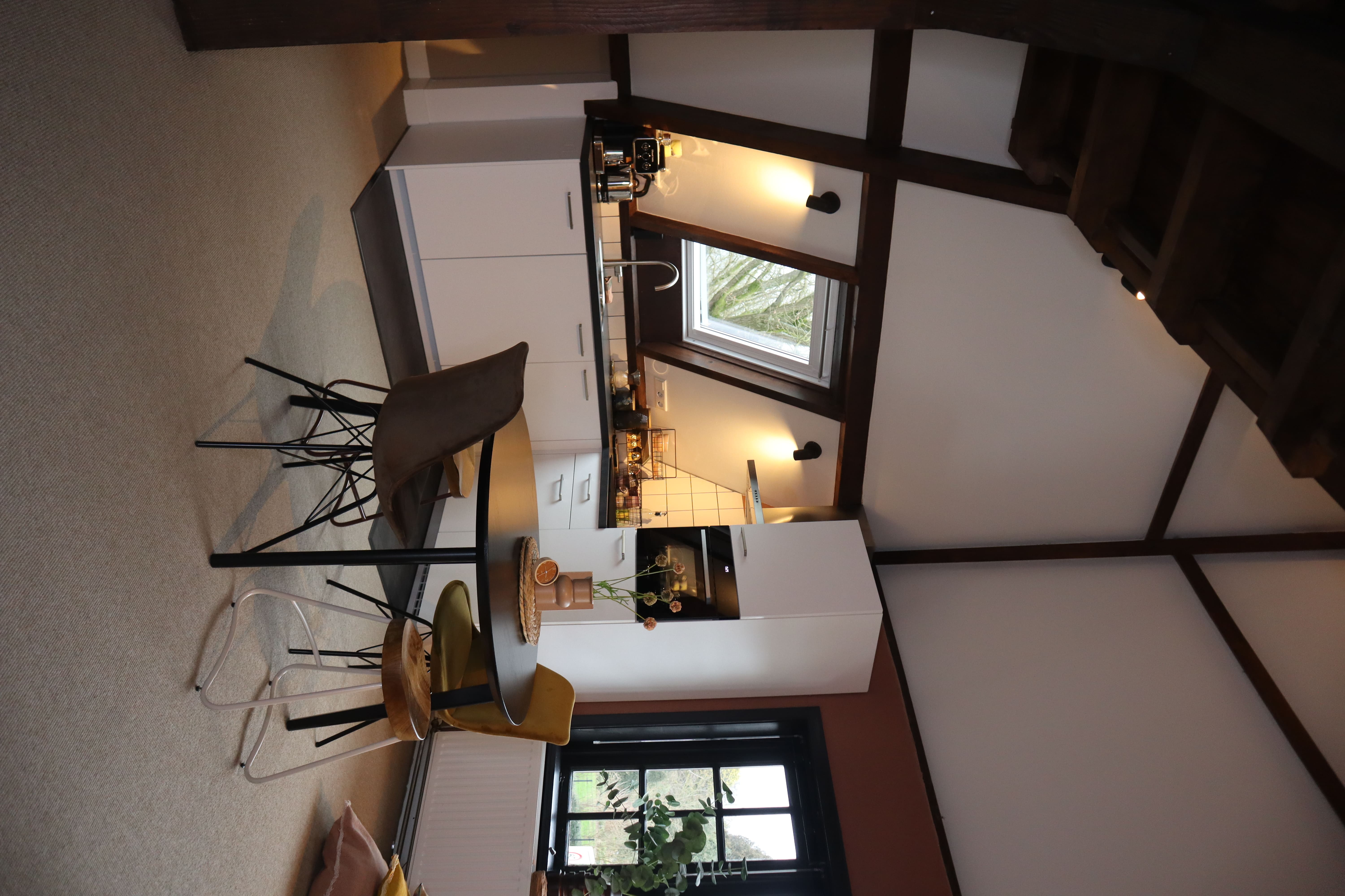 Moderne keuken met witte kasten, een fornuis, en een eettafel met stoelen. Het raam biedt uitzicht op de buitenomgeving en de kamer heeft houten balken.