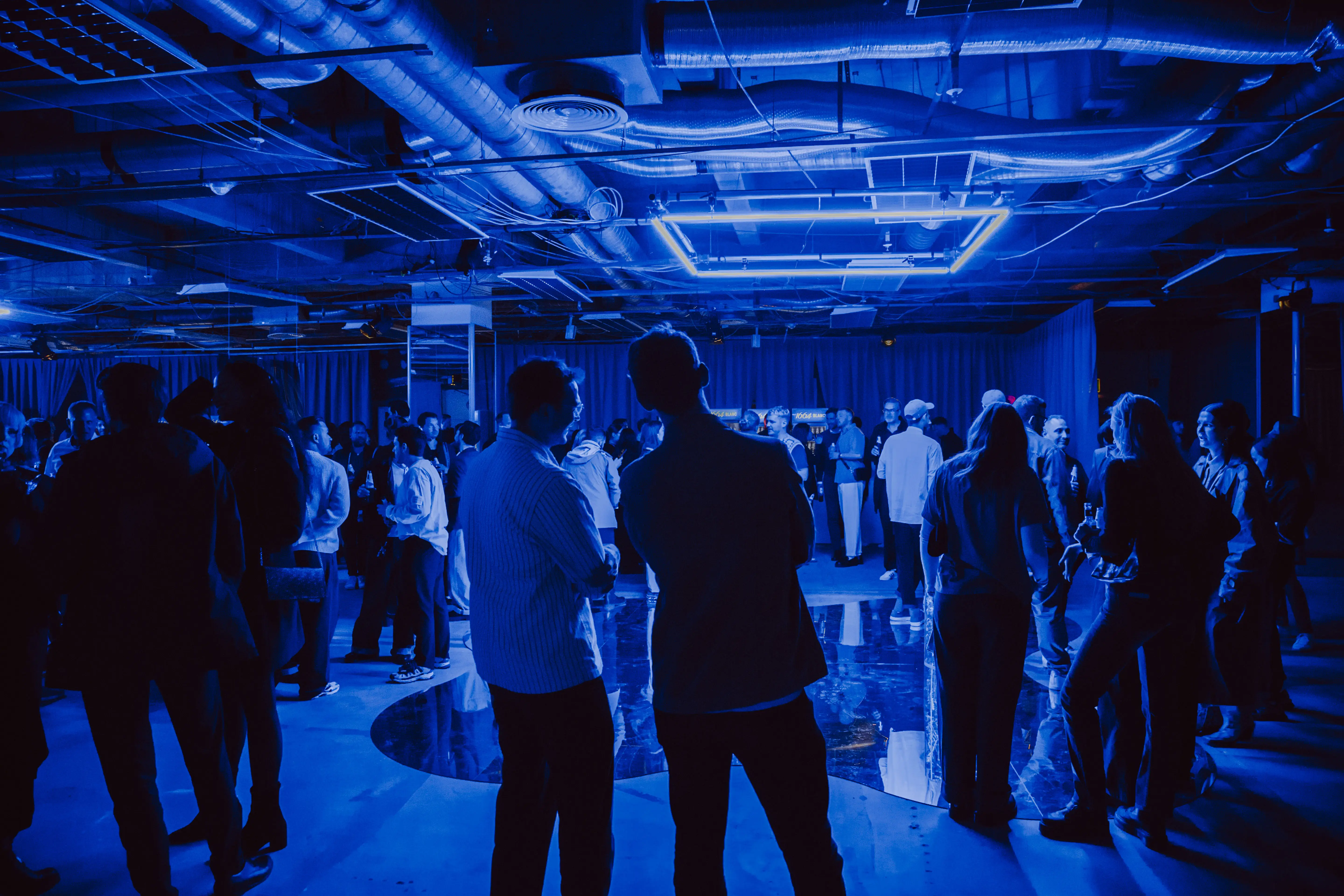 Guests in a blue-lit event space with neon ceiling frame and mirrored dance floor.
