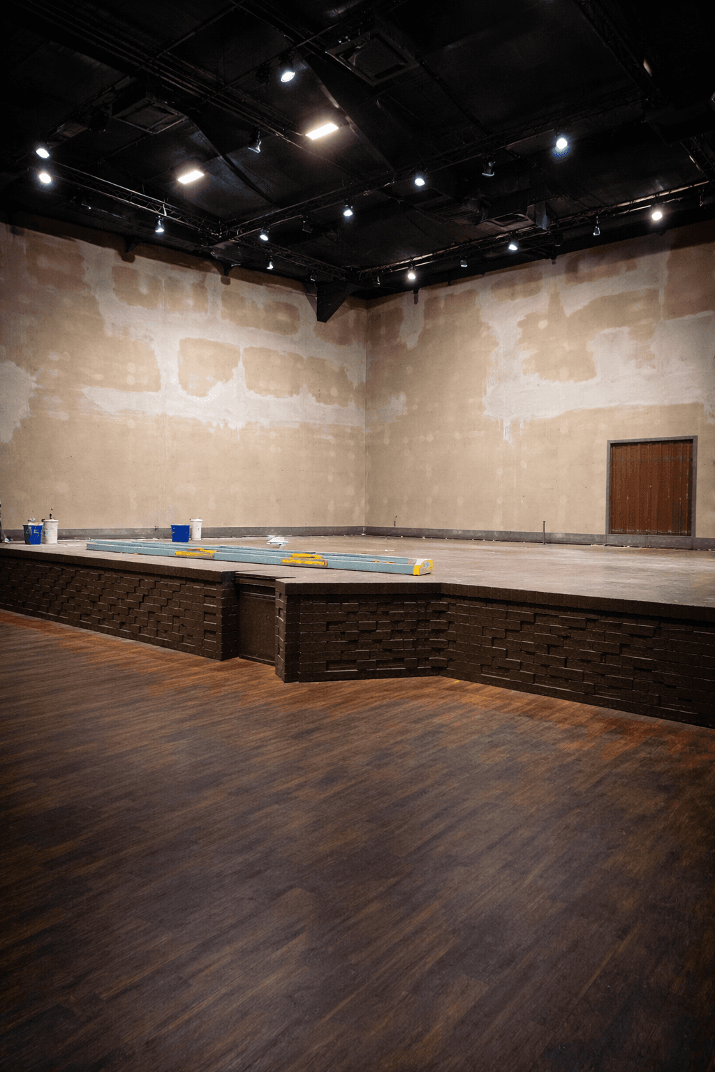 A modern, luxury beachfront villa with large glass windows and balconies overlooks a rocky shoreline, surrounded by palm trees at sunset.