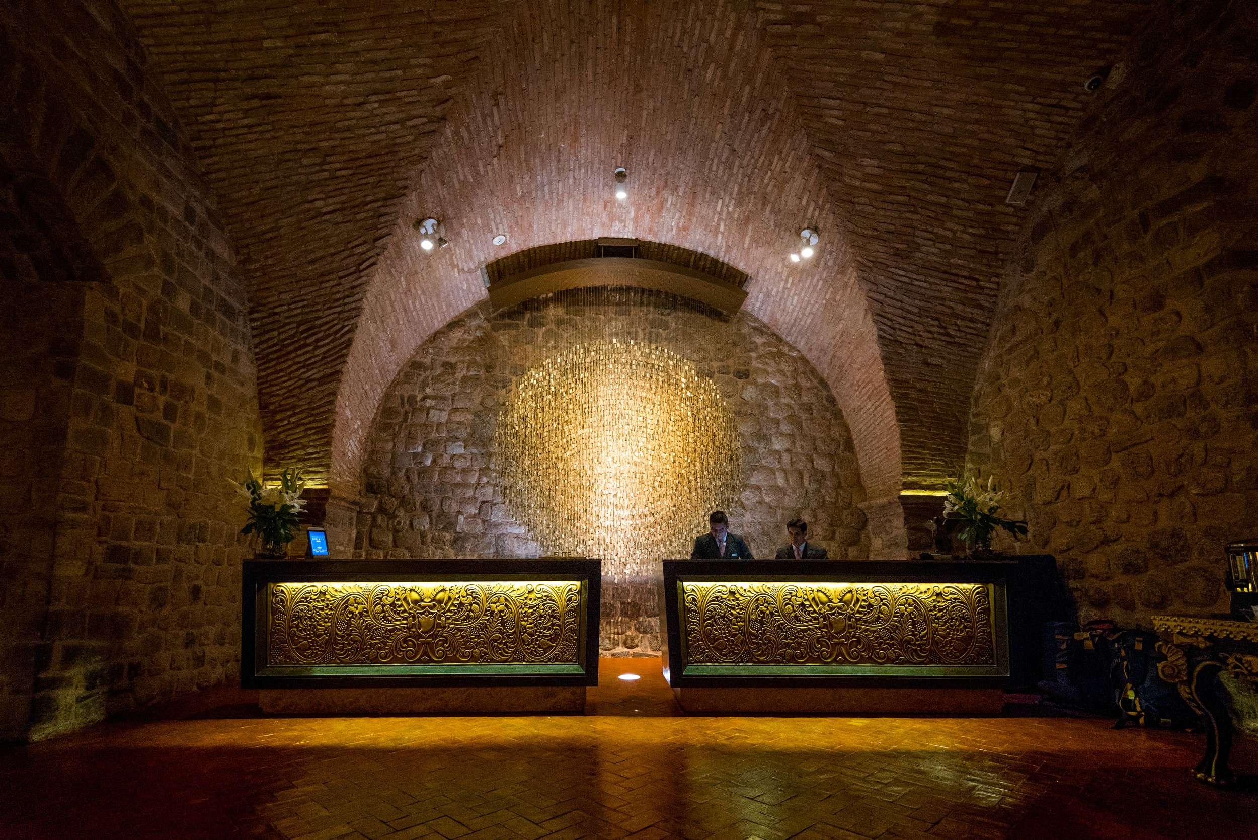 A stone vaulted cellar with two long wooden counters and a textured stone wall illuminated by warm overhead lights.
