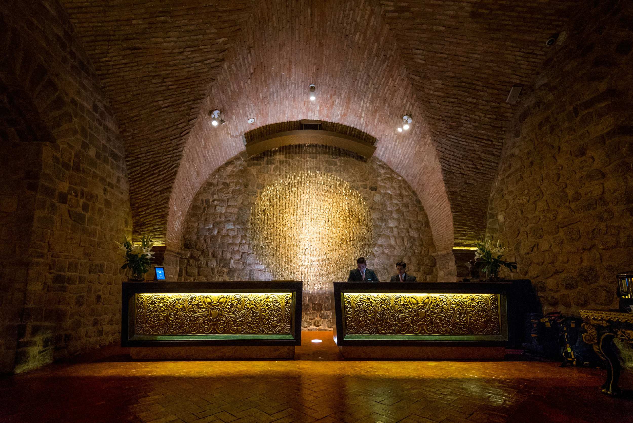 A stone vaulted cellar with two long wooden counters and a textured stone wall illuminated by warm overhead lights.