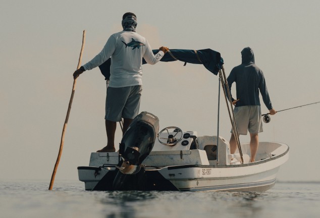 Fishing guide and angler on a skiff in Belize. Guide is poling the boat and scouting for fish.
