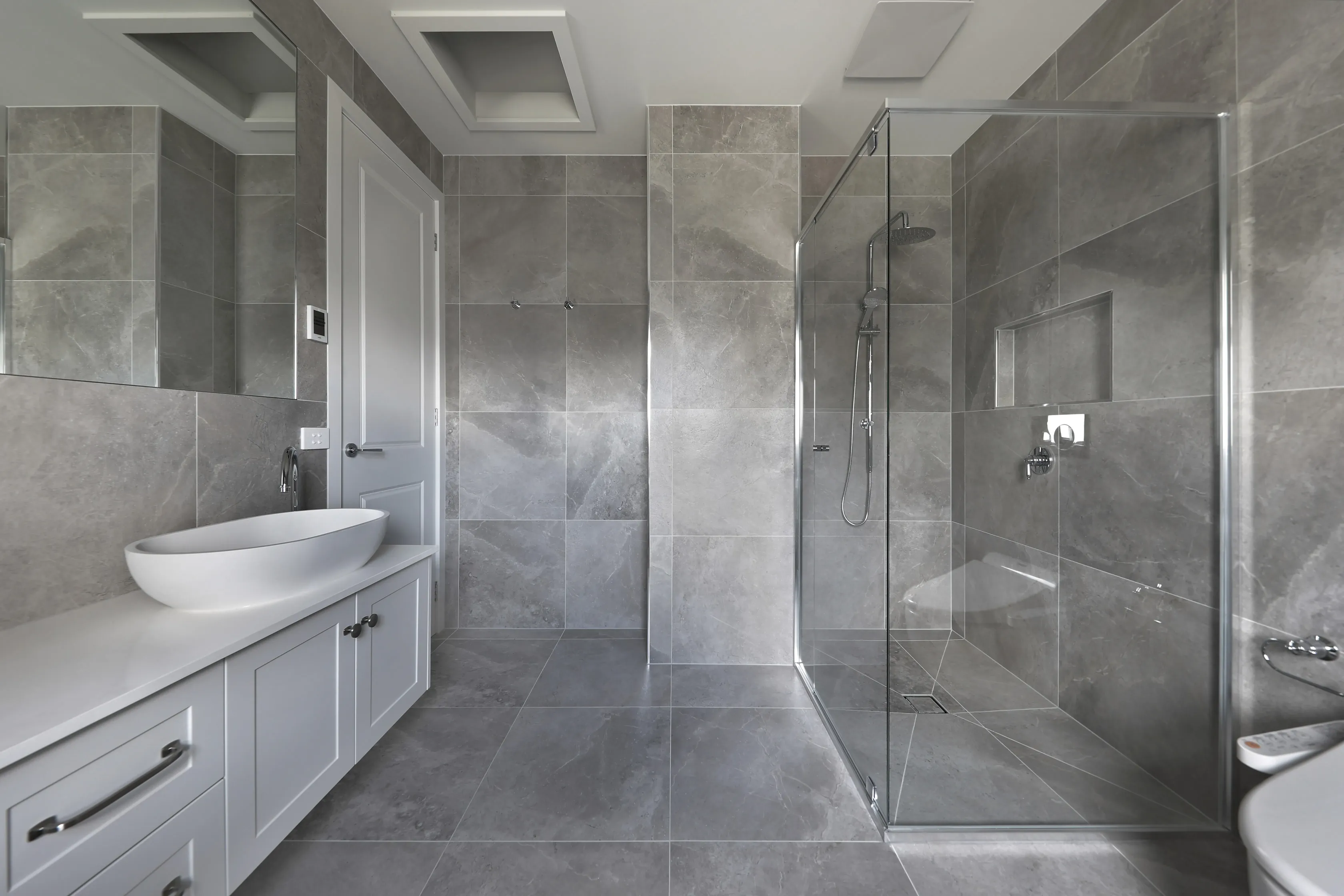 Ensuite bathroom in grey marble-look tiles with a frameless glass shower, rain head, white shaker vanity with a vessel basin and a large mirror