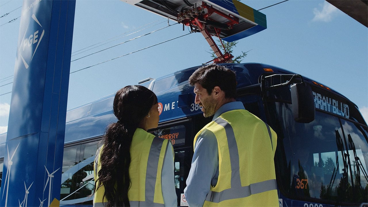 Two people in high-visibility jackets standing in front of an electric bus.