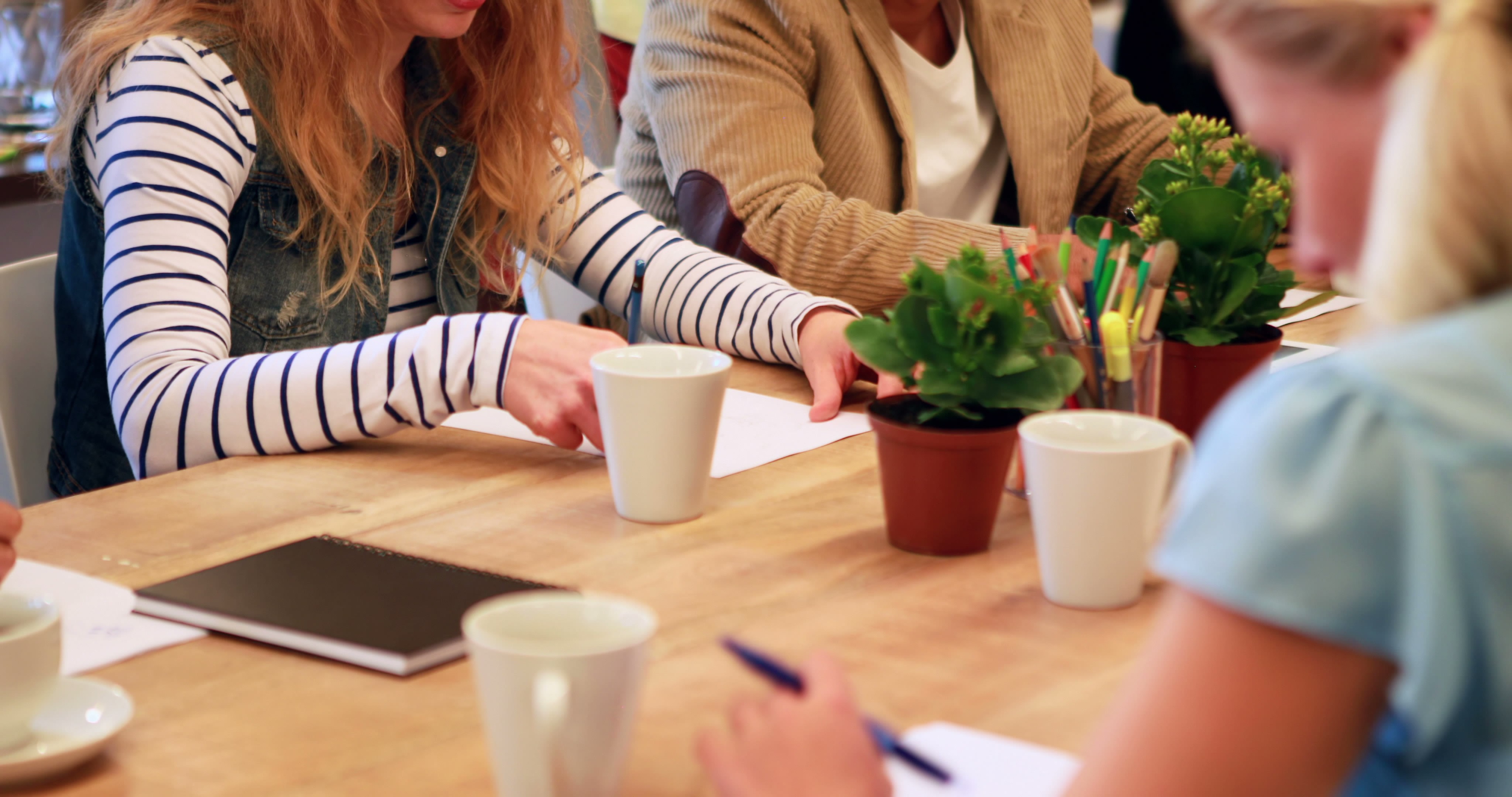 Group sitting at wooden table with coffee mugs focuses on common project.