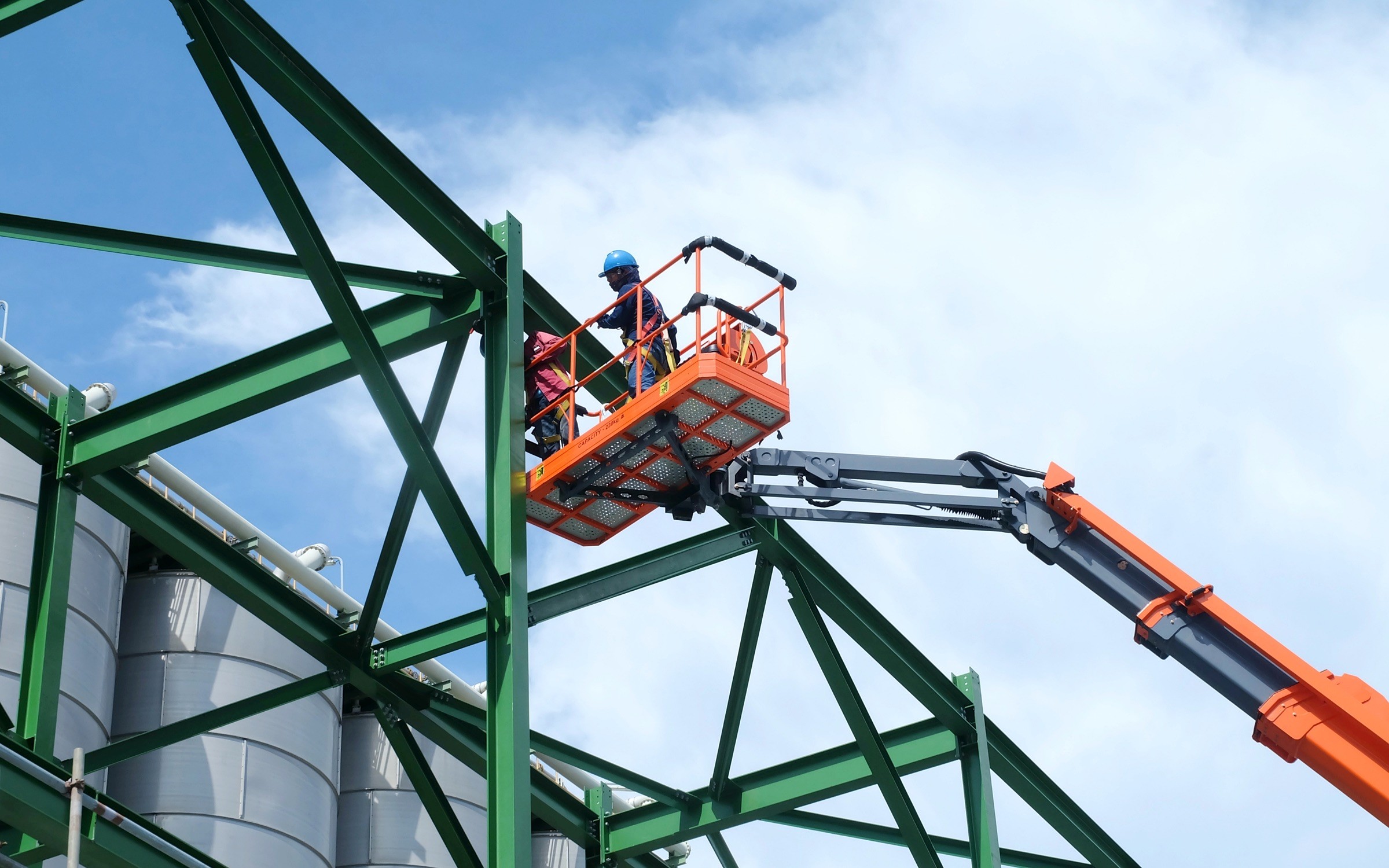 A photo of a construction workers in a boom lift working on the metal frame of a building.
