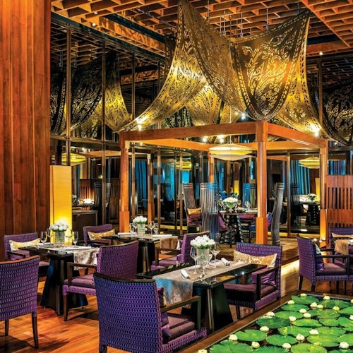 શ્રેણીકૃત રેસ્ટોરન્ટ, અજાર ચેરો સાથે, લાકડાના સજાવટ, કઠણ સોનાના છતના પેનલ અને સફેદ ફૂલ અને જલ્દીના સાપત્રી સાથે સુરવૈઝાકાર ટેબલ્સ.