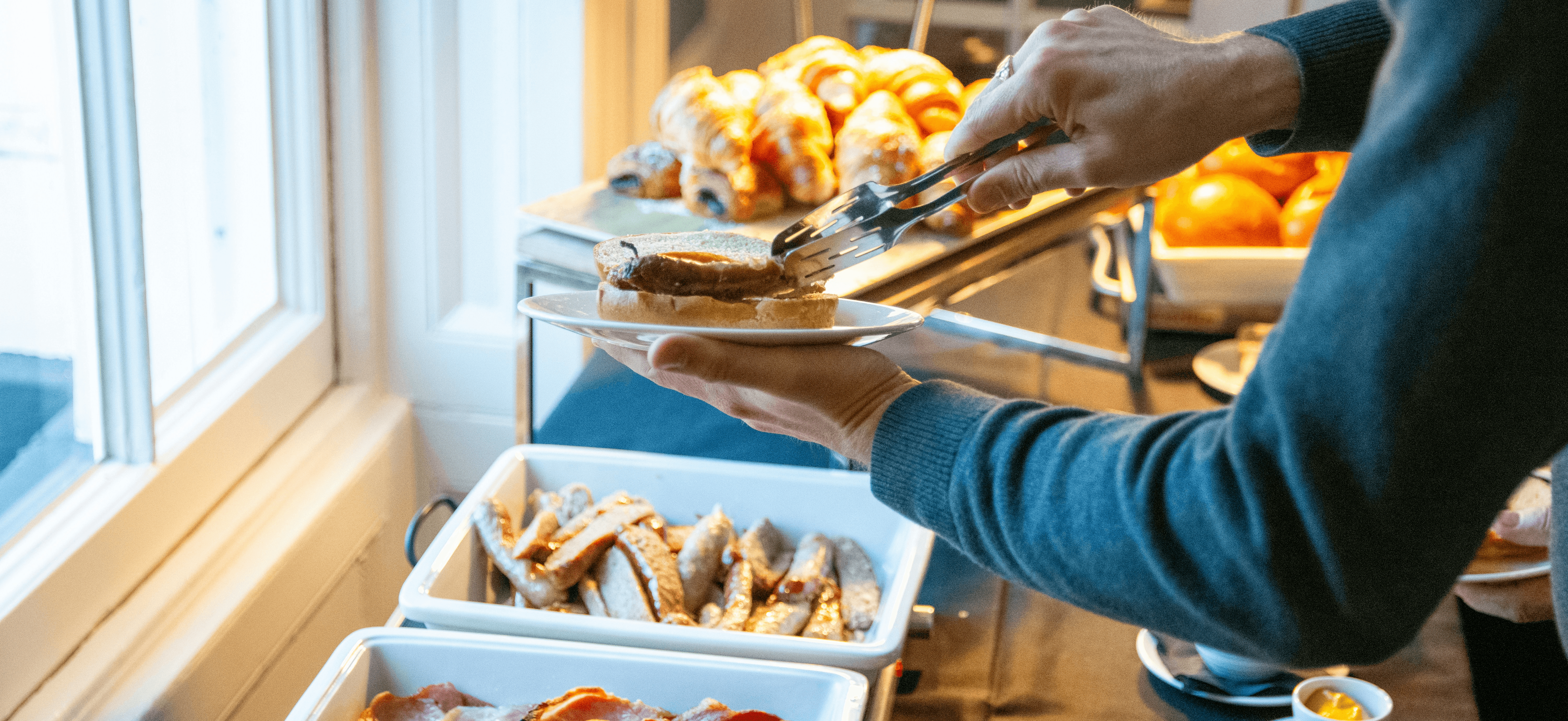 Person serving breakfast buffet with bacon and pastries
