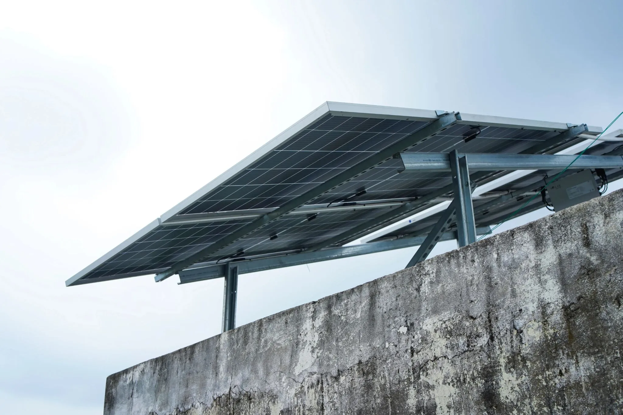 Solar panels on a raised steel frame above a concrete rooftop wall