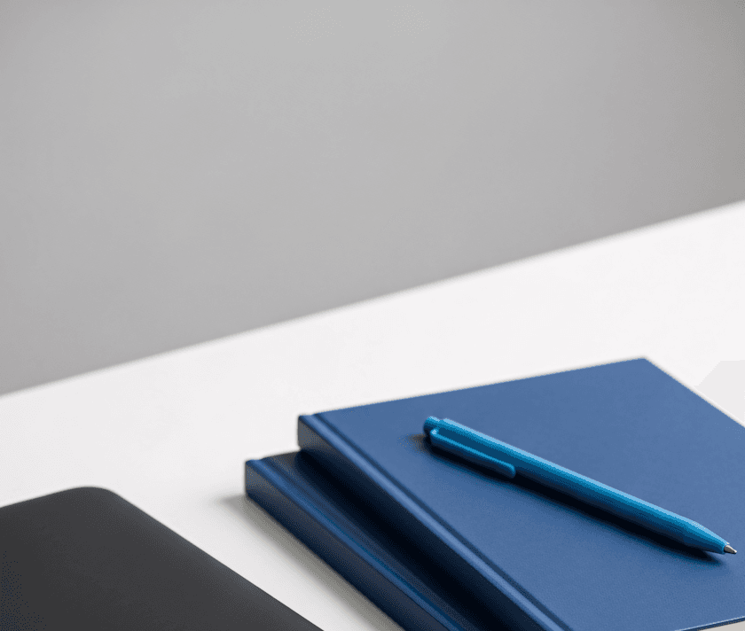 Close-up of a blue pen resting on a stack of navy blue notebooks on a minimalist