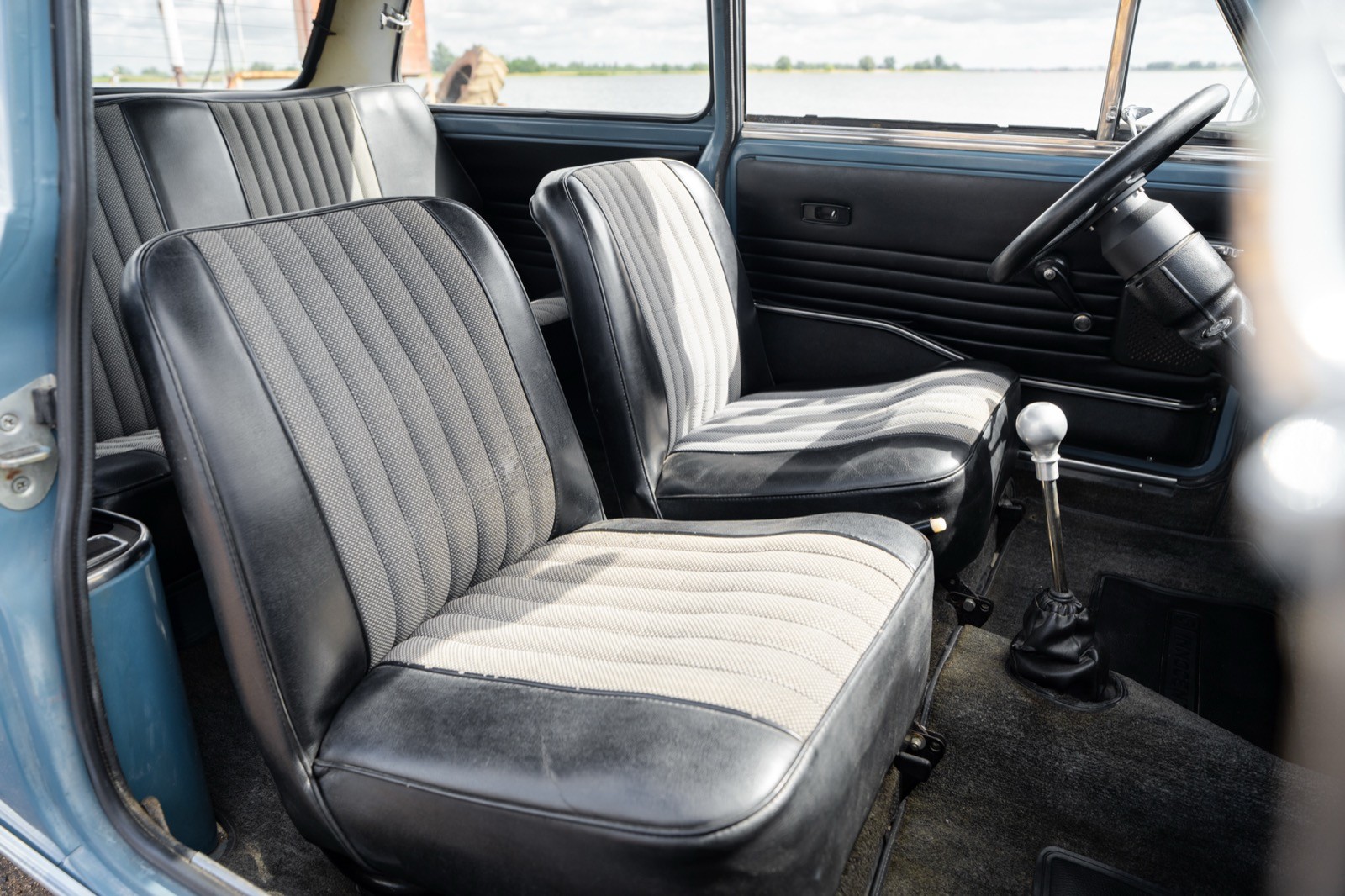Interior view of a vintage car showing two front seats and dashboard, with a classic design and simple upholstery.