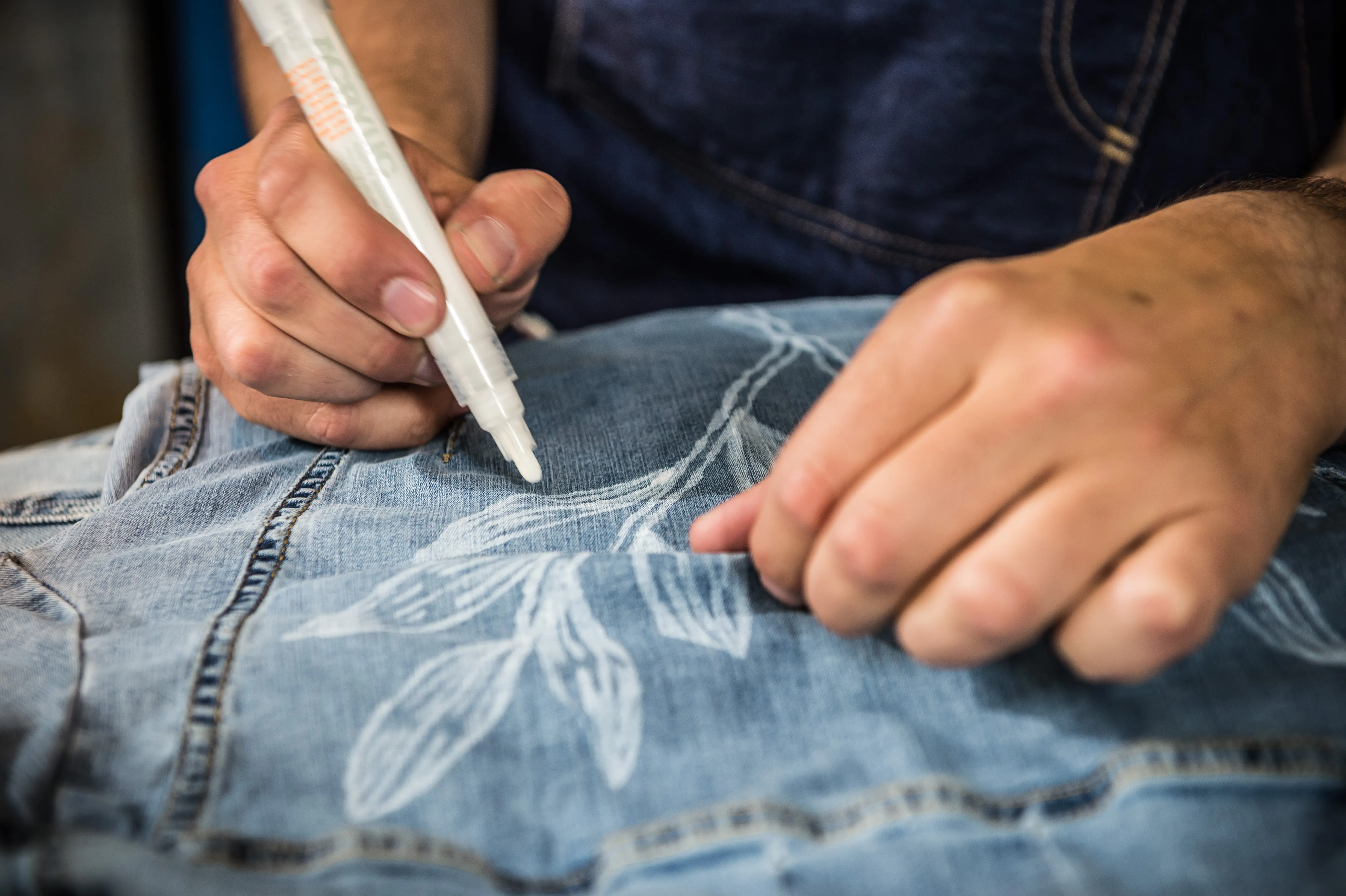 Close-up of hands drawing a white leaf pattern onto denim with a paint marker at the MUSTANG Street ART Lab.
