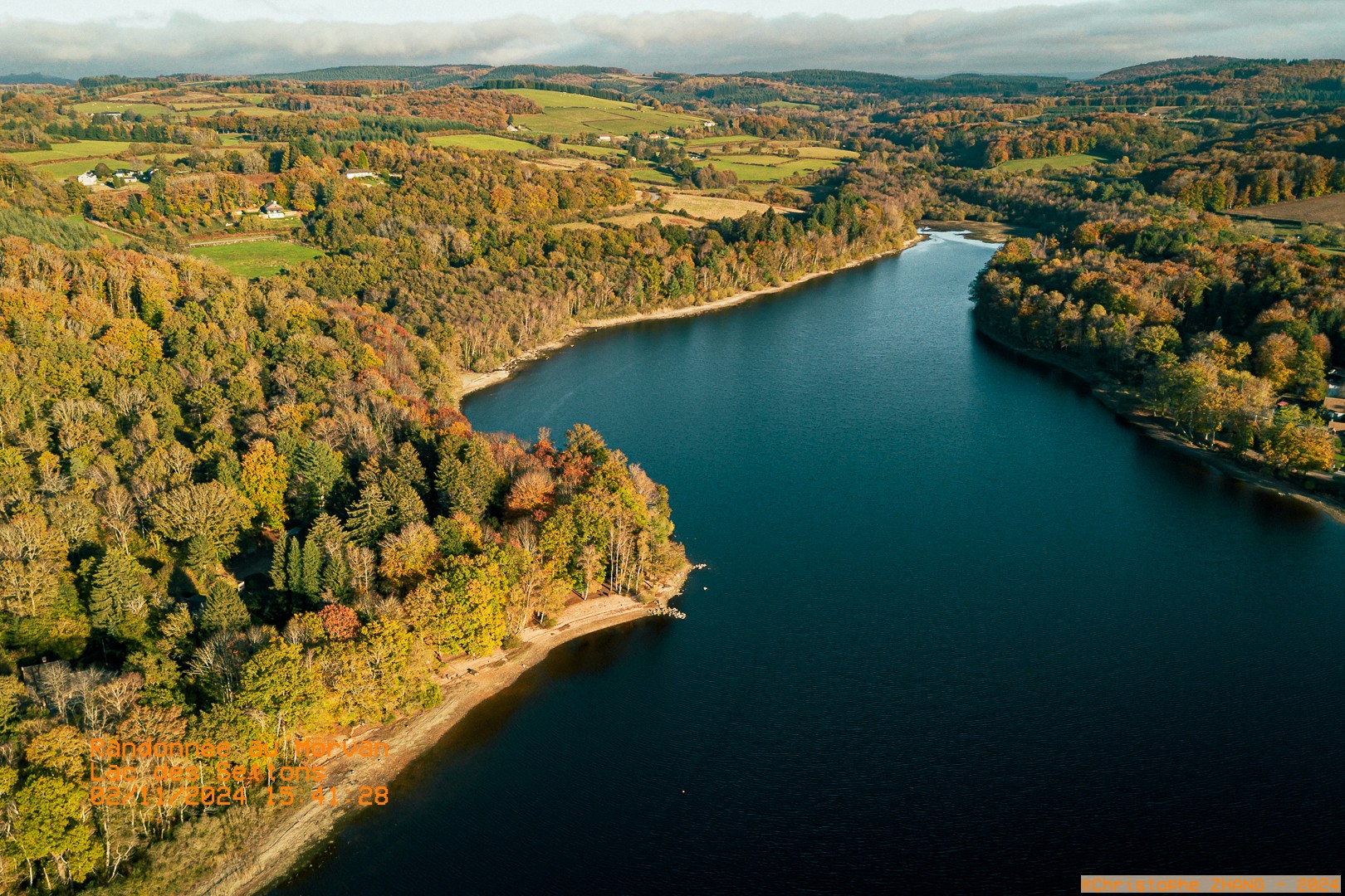 Vue aérienne d’un lac des Settons bordé de forêts et de collines verdoyantes dans le Morvan.