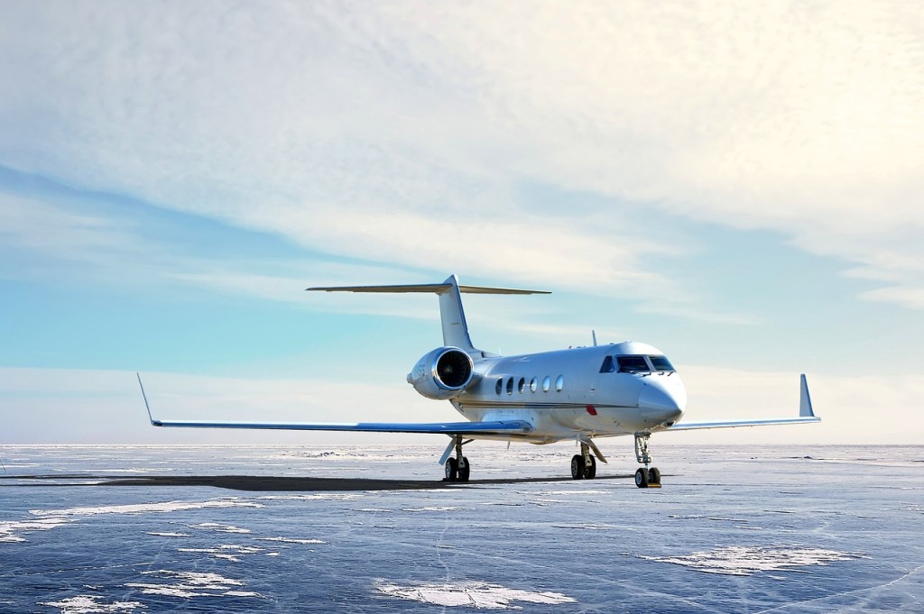 Private jet parked on a snow-covered runway under a clear blue sky, showcasing the sleek design and powerful engines of a modern luxury aircraft