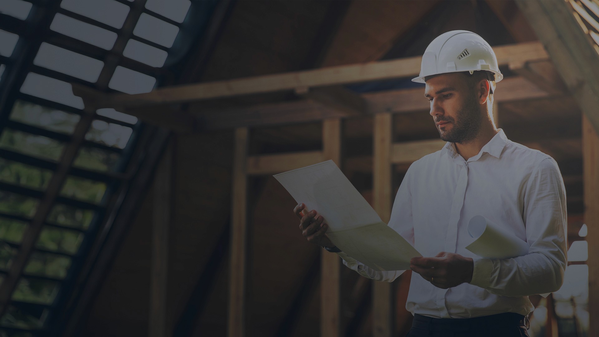 Engenheiro usando capacete branco e analisando planta de projeto em uma obra em estrutura de madeira.