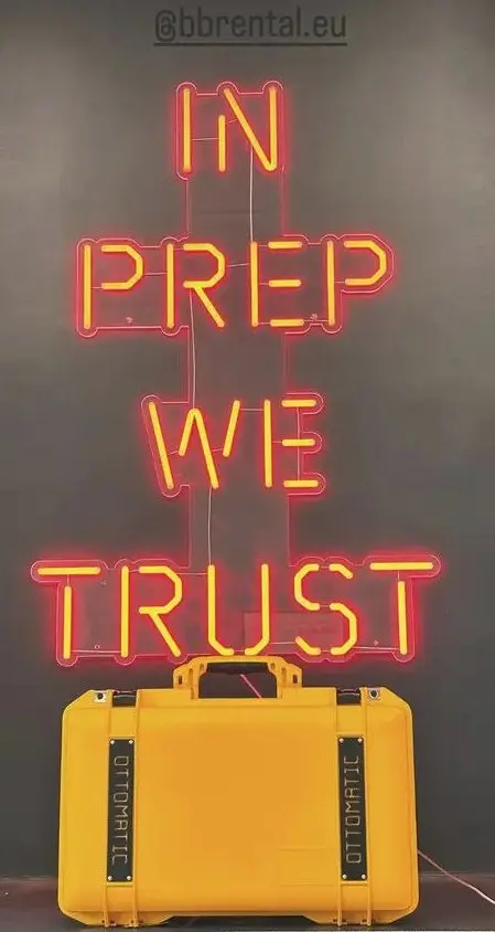Yellow Pixel Cube case beneath an IN PREP WE TRUST neon sign.