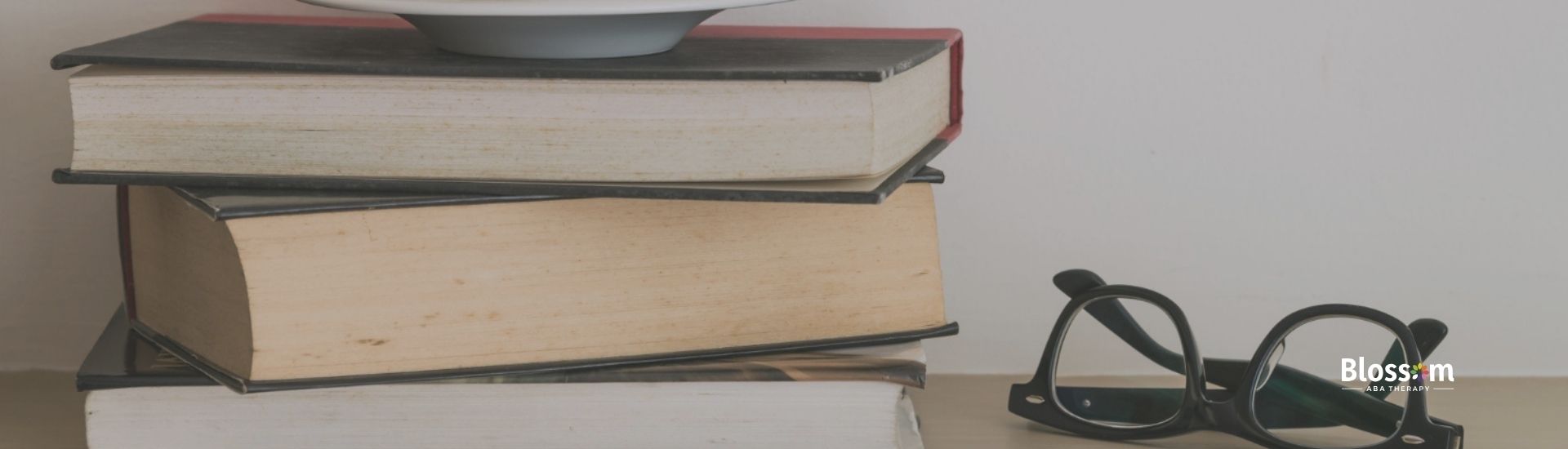 Stack of books about ABA therapy with a coffee cup and glasses.