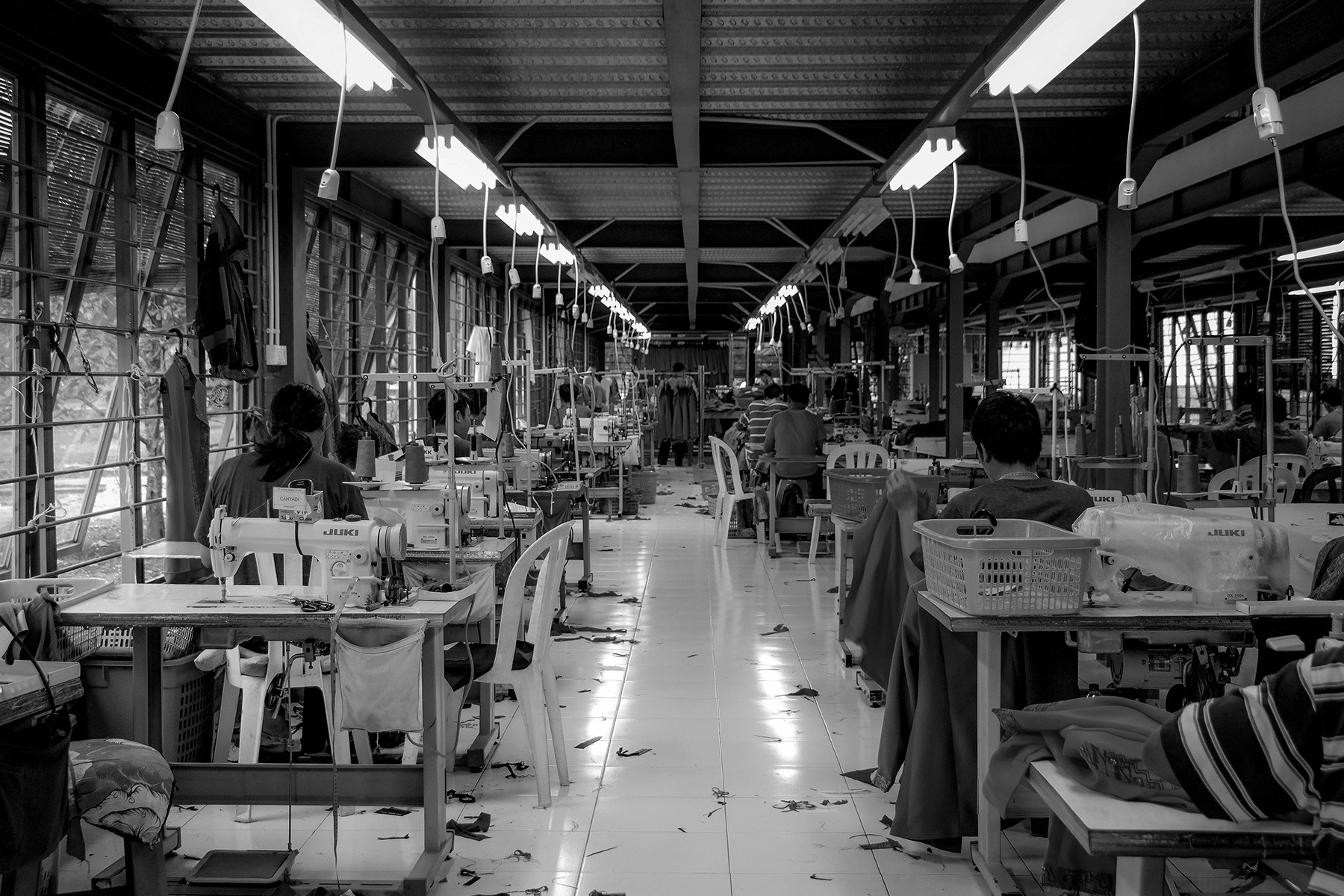 A black-and-white photo of a spacious workshop with people working at various benches and machinery.