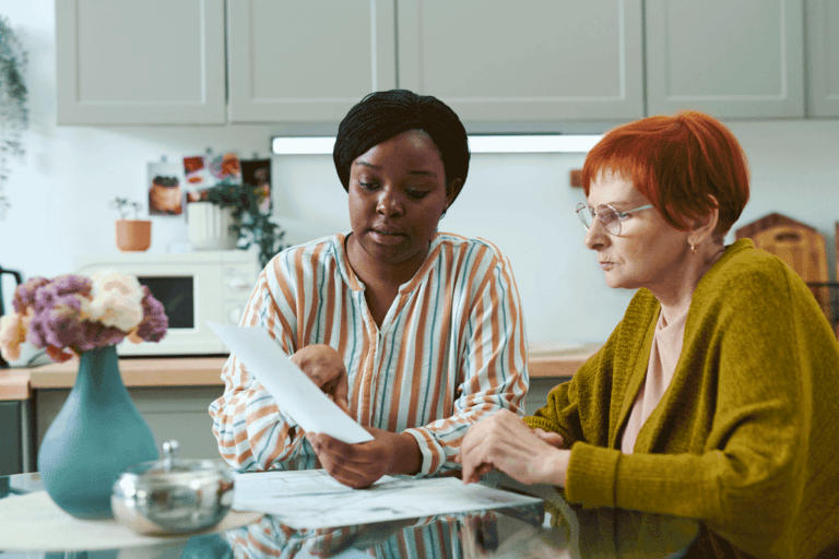 A caregiver and an elderly woman sitting together reviewing documents, representing personalised care and support planning in social care
