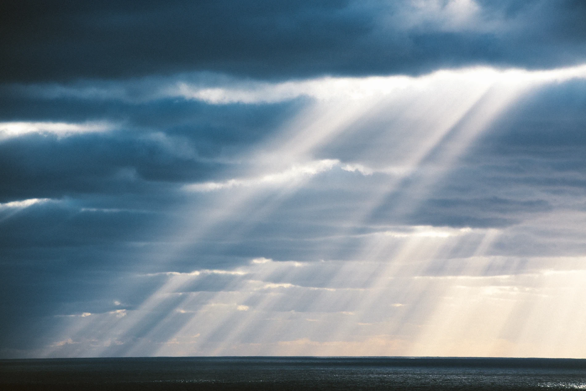 Shafts of sunlight breaking through heavy cloud over a dark sea