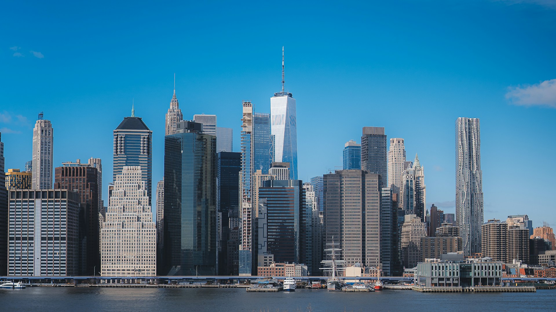 Lower Manhattan skyline with One World Trade Center reflected across the East River.