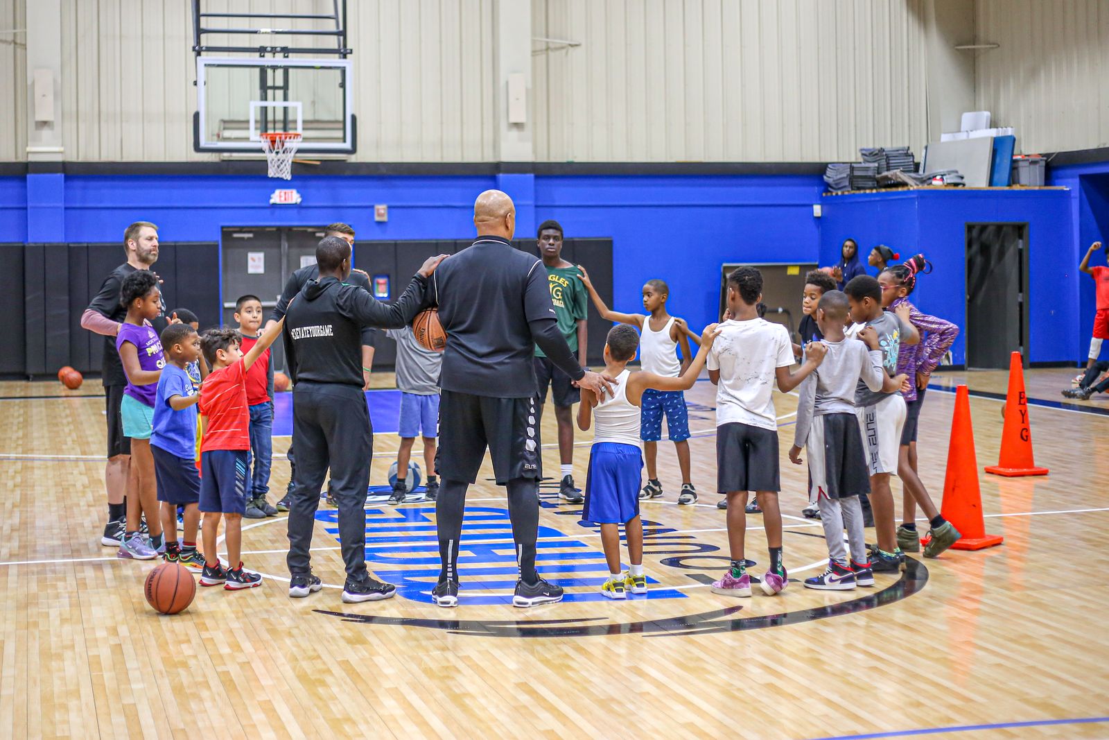 Group of kids in a basketball gym huddling with coaches.