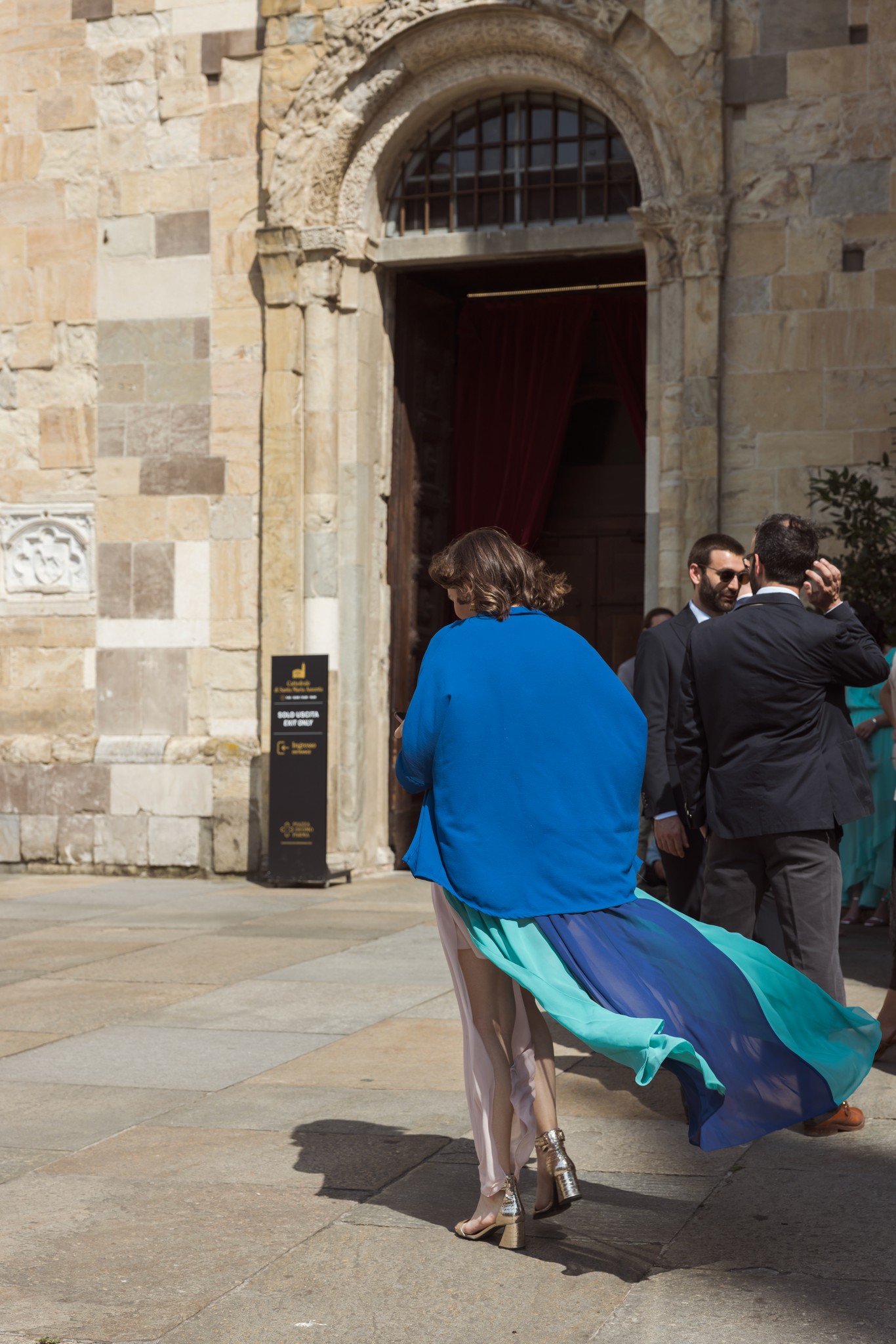 Sposa in abito blu che varca la porta di pietra della chiesa, accompagnata da familiari durante la cerimonia matrimoniale