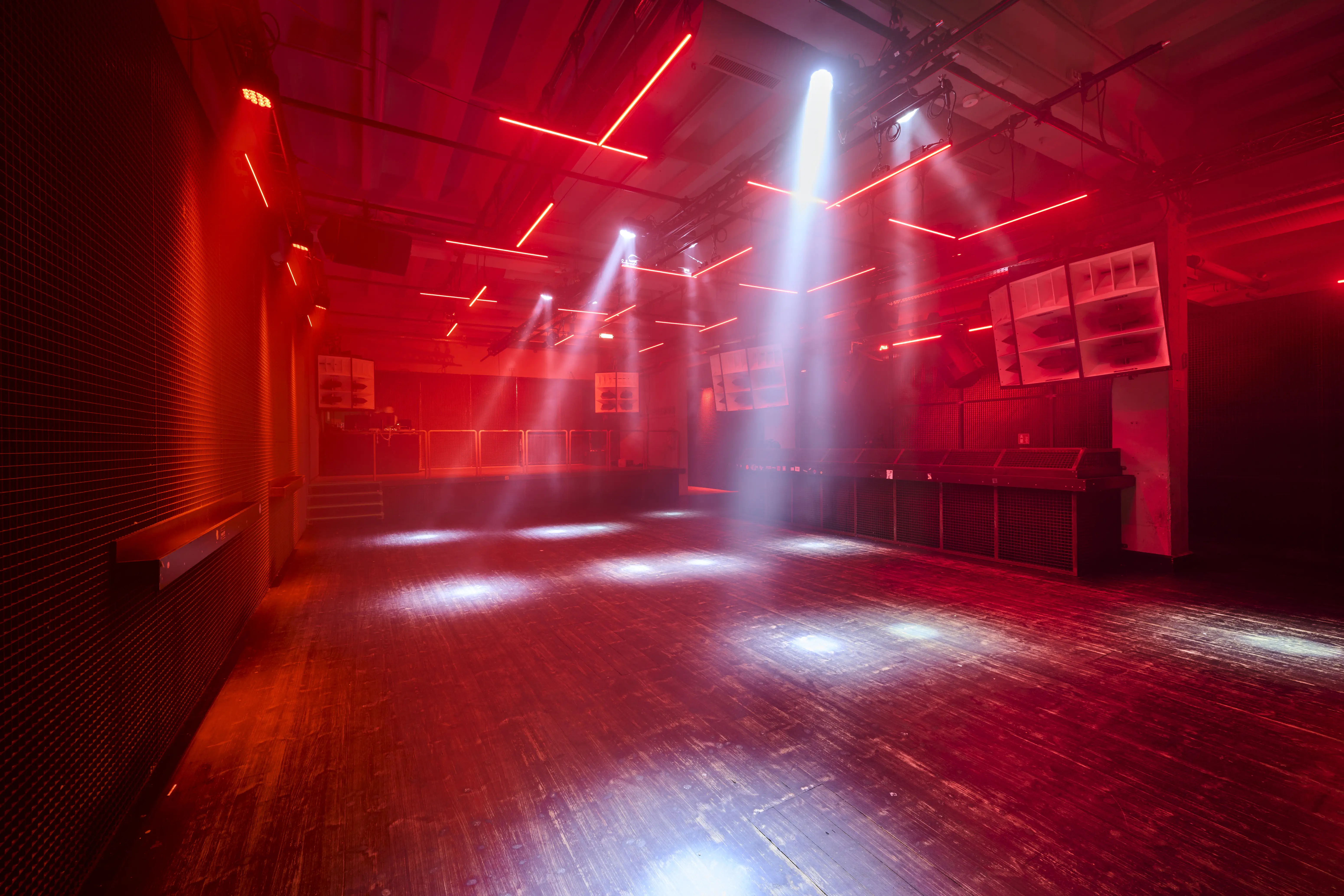 Red-lit dancefloor at TRESOR GLOBUS with haze and spotlight beams, red neon lines on the ceiling, dark wooden floor and speaker cabinets along the walls.