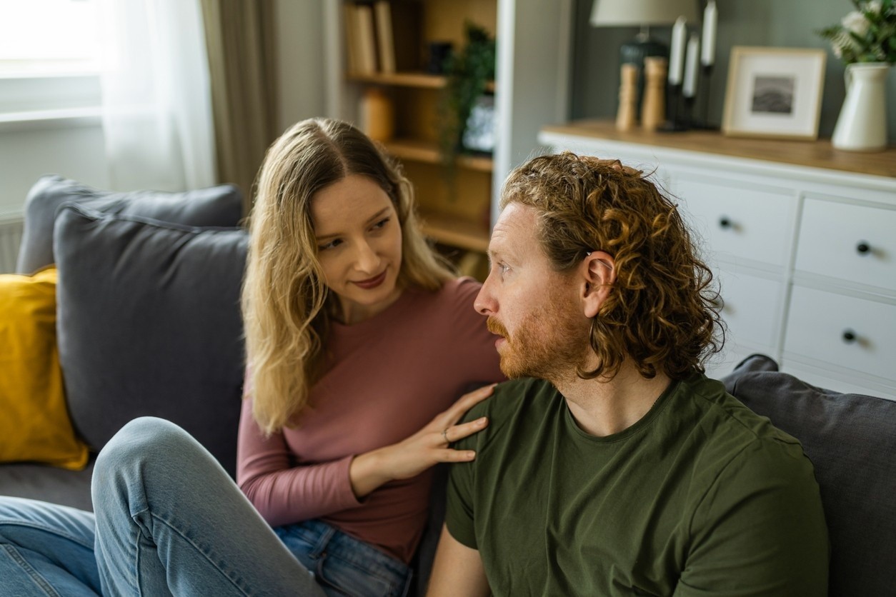 Woman placing a hand on a man's shoulder while sitting together on a couch