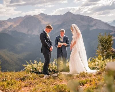 The couple look down as the officiant reads from an open book at the mountain ceremony.